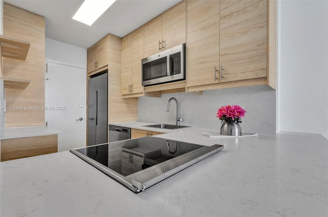 kitchen with a sink, appliances with stainless steel finishes, light brown cabinetry, backsplash, and light stone counters