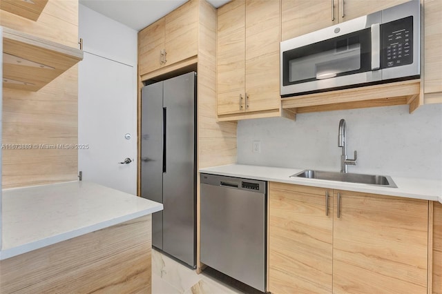 kitchen with stainless steel appliances, light countertops, a sink, and light brown cabinetry