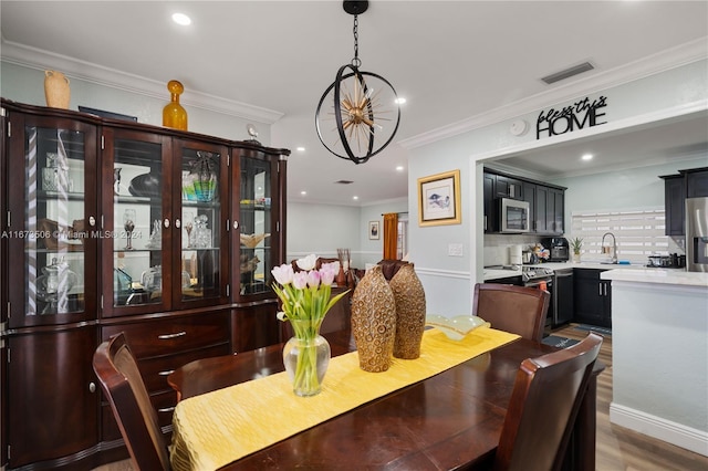 dining space featuring sink, crown molding, hardwood / wood-style floors, and a chandelier