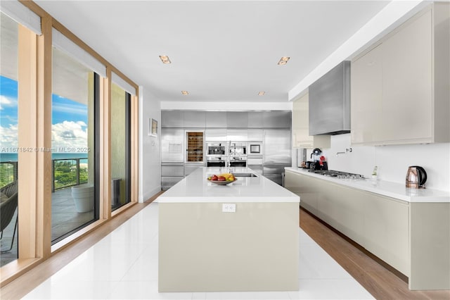 kitchen featuring stainless steel gas stovetop, light tile patterned floors, gray cabinets, a center island, and wall chimney range hood