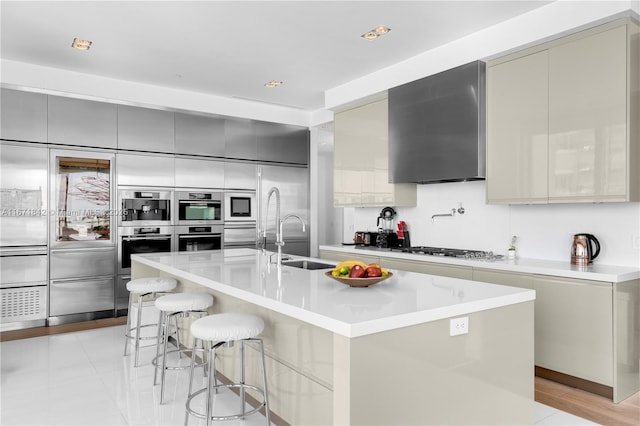 kitchen with gray cabinets, a breakfast bar, double oven, and a center island with sink