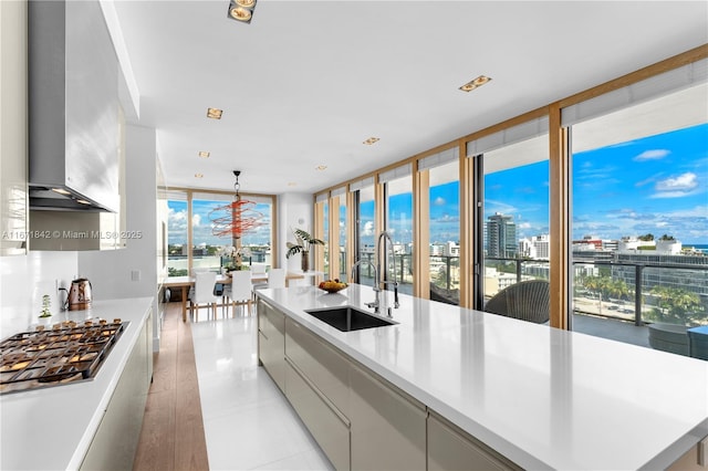 kitchen featuring stainless steel gas stovetop, hanging light fixtures, light tile patterned floors, sink, and a large island with sink