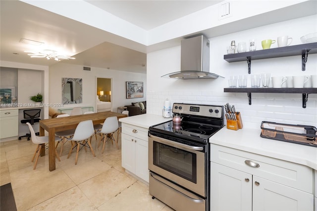 kitchen with wall chimney exhaust hood, ceiling fan, stainless steel electric range oven, and white cabinetry