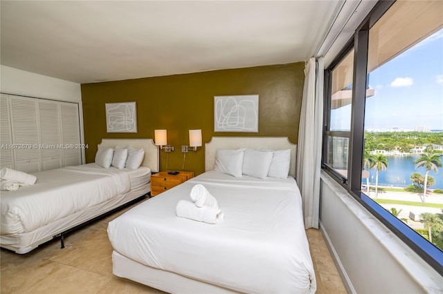 tiled bedroom with a water view, multiple windows, and a closet