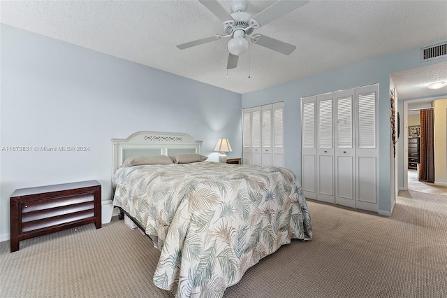 carpeted bedroom featuring ceiling fan, multiple closets, and a textured ceiling