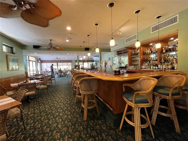 bar with dark carpet, decorative light fixtures, a textured ceiling, and ceiling fan