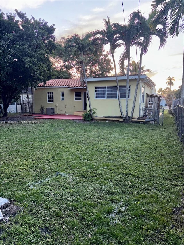 back house at dusk with a patio, a yard, and central air condition unit