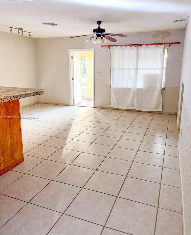 tiled empty room with a healthy amount of sunlight, track lighting, and ceiling fan