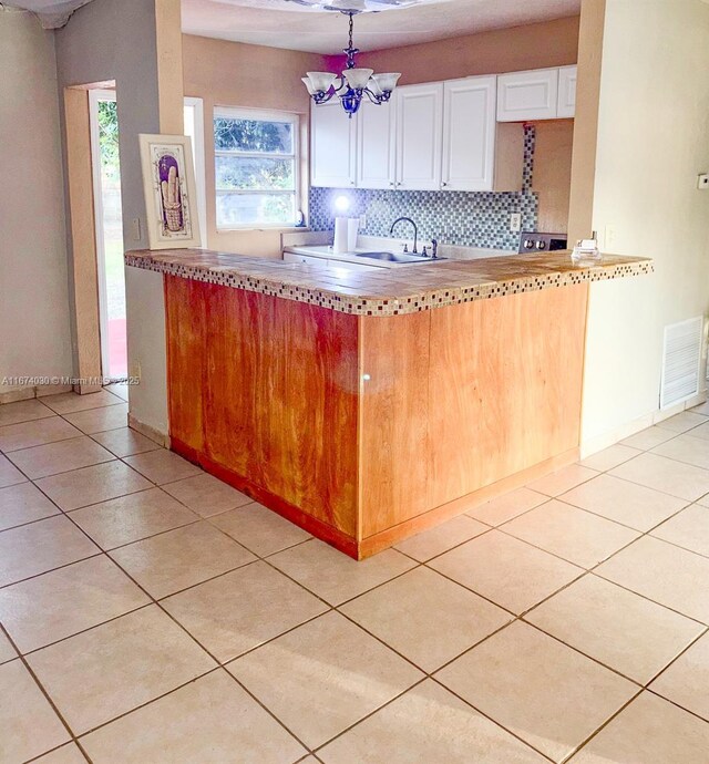 kitchen with pendant lighting, light tile patterned floors, white cabinetry, a notable chandelier, and decorative backsplash