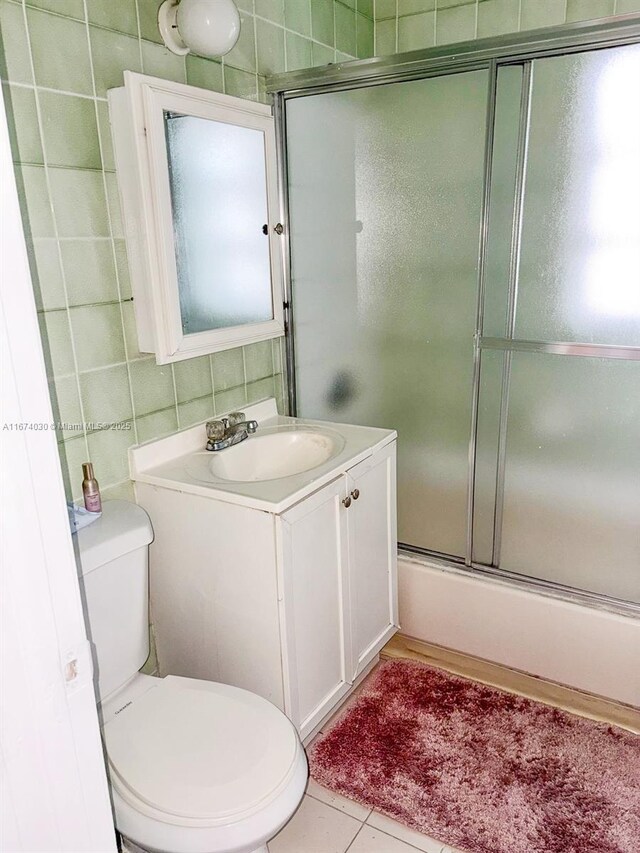 full bathroom featuring tile walls, enclosed tub / shower combo, vanity, toilet, and tile patterned floors