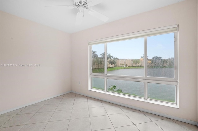 empty room with ceiling fan, light tile patterned floors, and a water view