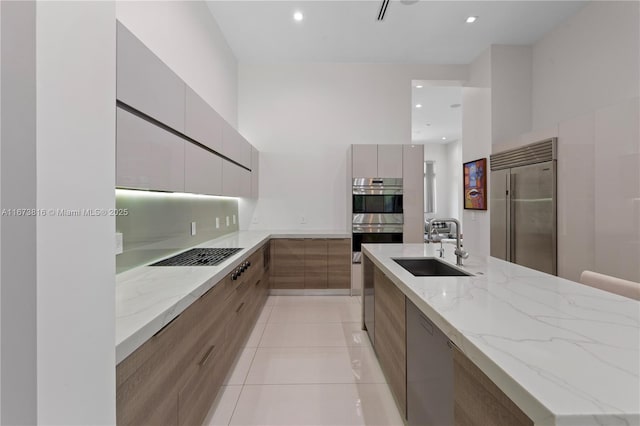 kitchen with appliances with stainless steel finishes, sink, decorative backsplash, light tile patterned floors, and light stone counters