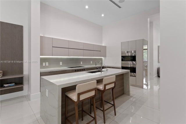 kitchen with gray cabinets, an island with sink, sink, a breakfast bar area, and stainless steel appliances