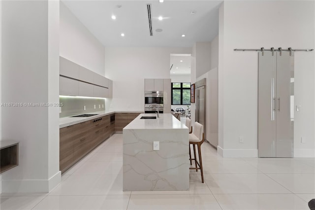 kitchen featuring a breakfast bar, sink, black electric stovetop, light stone counters, and a center island with sink