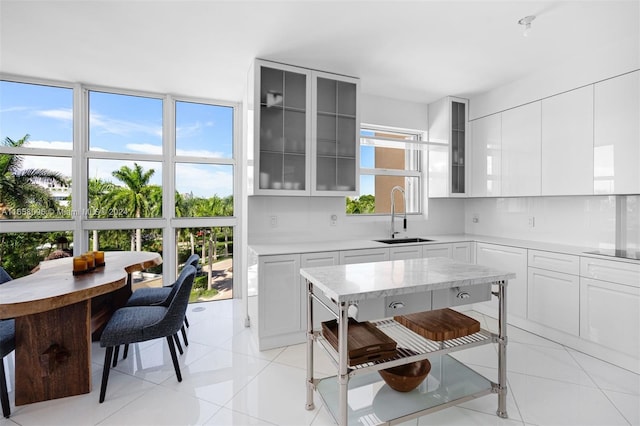 kitchen featuring black electric stovetop, sink, backsplash, white cabinets, and light tile patterned floors