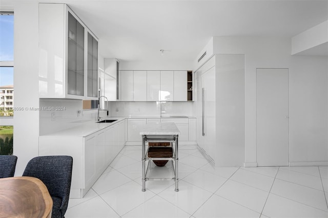 kitchen featuring backsplash, light tile patterned flooring, sink, and white cabinets