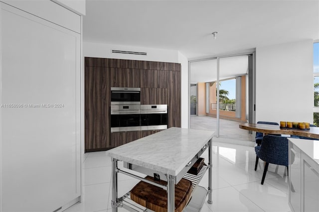 kitchen with stainless steel double oven, dark brown cabinets, and light tile patterned floors