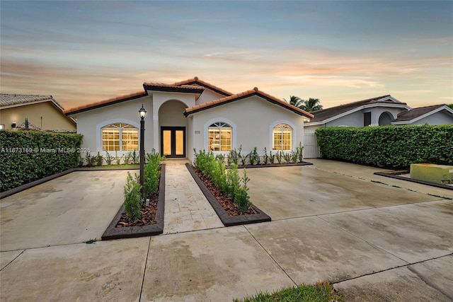 mediterranean / spanish house featuring driveway, french doors, stucco siding, fence, and a tiled roof