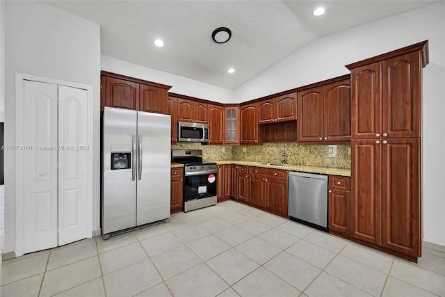 kitchen featuring backsplash, vaulted ceiling, appliances with stainless steel finishes, light stone counters, and a textured ceiling