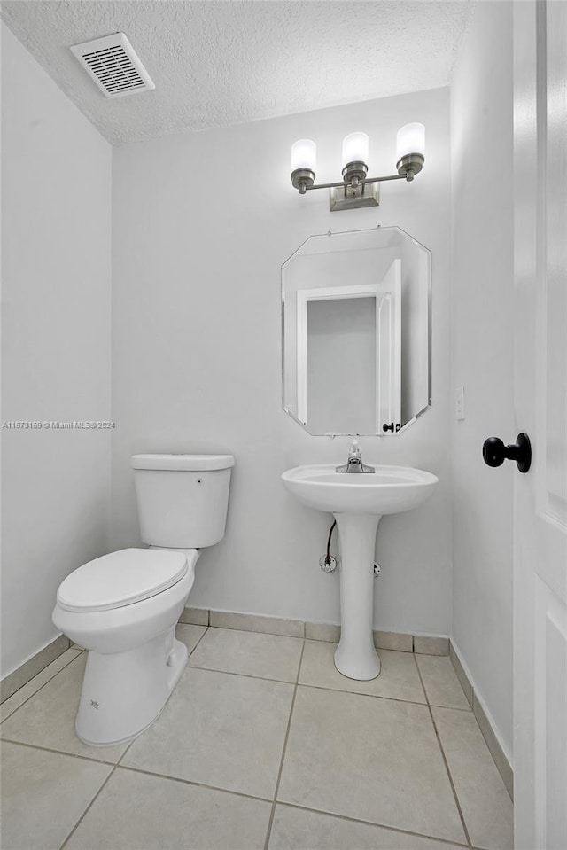 bathroom with toilet, a textured ceiling, and tile patterned flooring