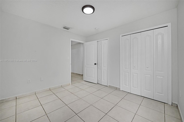 unfurnished bedroom with a textured ceiling, multiple closets, and light tile patterned floors