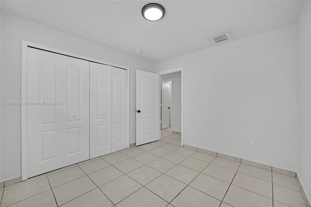 unfurnished bedroom with a closet, a textured ceiling, and light tile patterned flooring