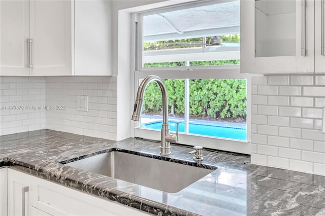 kitchen with a healthy amount of sunlight, dark stone counters, white cabinets, and a sink