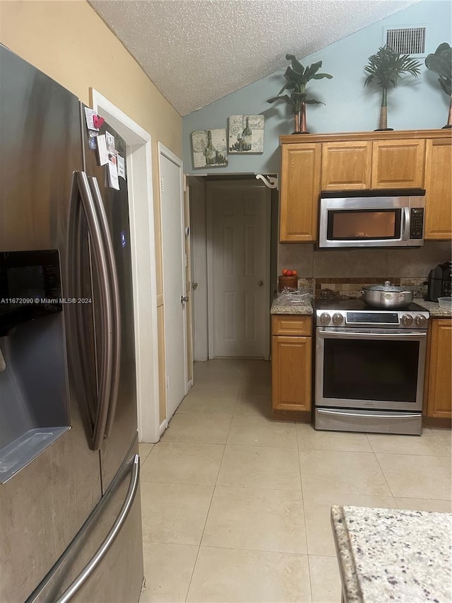 kitchen featuring light tile patterned floors, vaulted ceiling, stainless steel appliances, and a textured ceiling