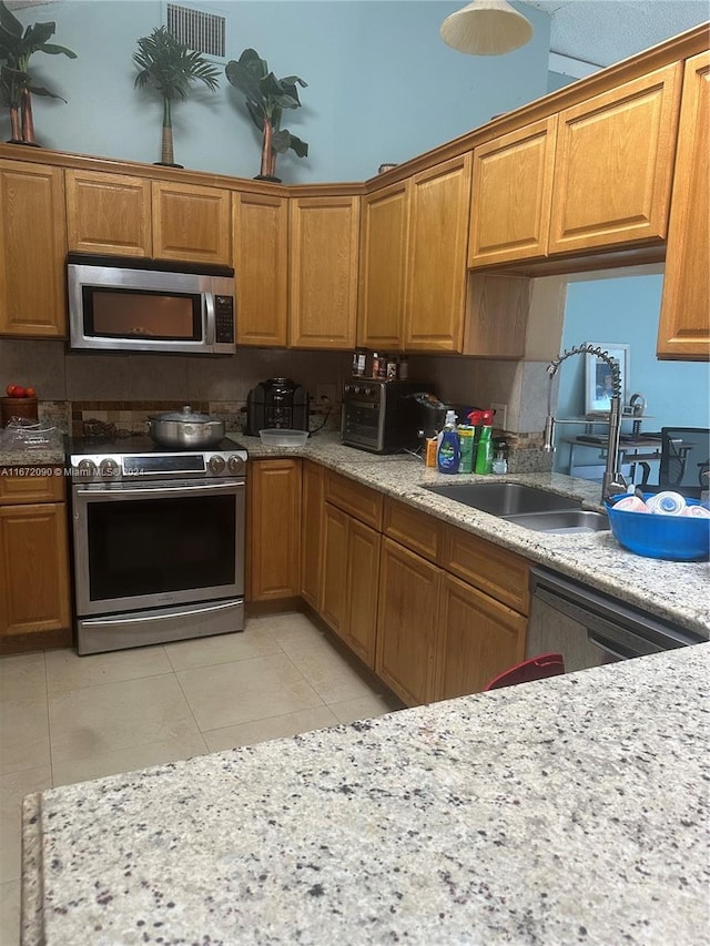 kitchen featuring light stone counters, light tile patterned floors, stainless steel appliances, and sink