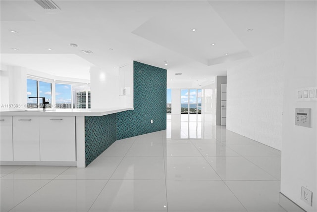 interior space with a tray ceiling, sink, light tile patterned floors, and white cabinetry