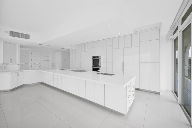 kitchen featuring stainless steel double oven, white cabinetry, sink, and a large island