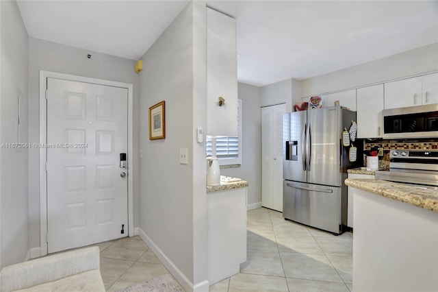 kitchen with light tile patterned floors, light stone counters, stainless steel appliances, and white cabinets