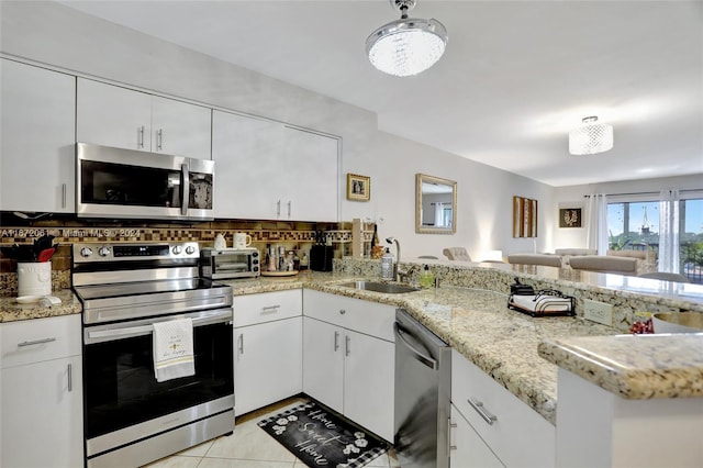 kitchen with white cabinets, sink, kitchen peninsula, appliances with stainless steel finishes, and light tile patterned floors