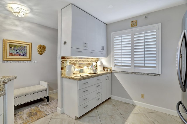 kitchen with stainless steel refrigerator, light stone countertops, white cabinets, and light tile patterned floors