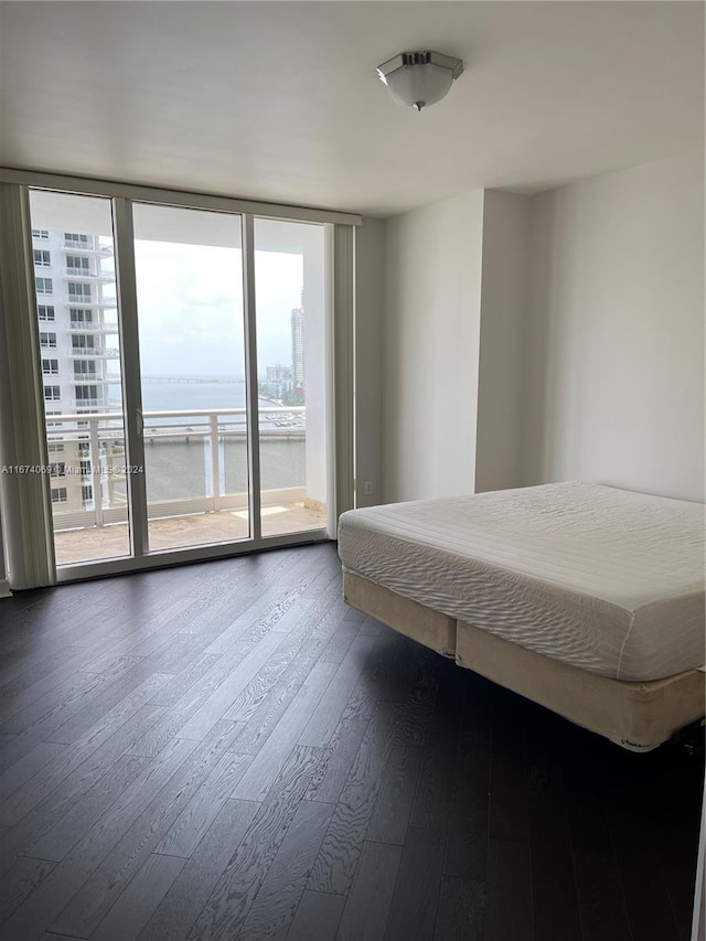 unfurnished bedroom featuring dark hardwood / wood-style floors, multiple windows, access to exterior, and a water view