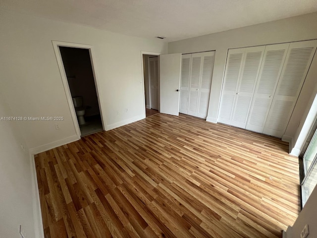 unfurnished bedroom featuring light wood-type flooring, two closets, and connected bathroom