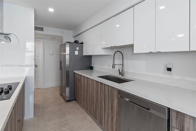 kitchen with white cabinetry, sink, light stone countertops, and appliances with stainless steel finishes