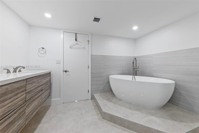 bathroom with a bathing tub, vanity, and tile walls