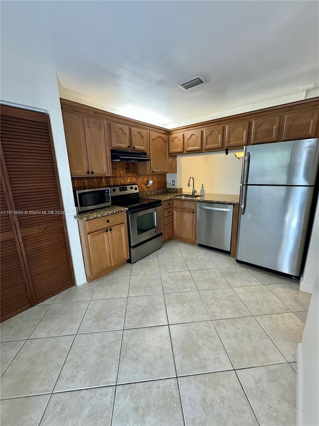 kitchen with light tile patterned flooring, sink, appliances with stainless steel finishes, dark stone countertops, and decorative backsplash