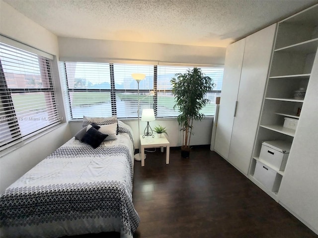 bedroom with a textured ceiling, dark wood-type flooring, and a water view