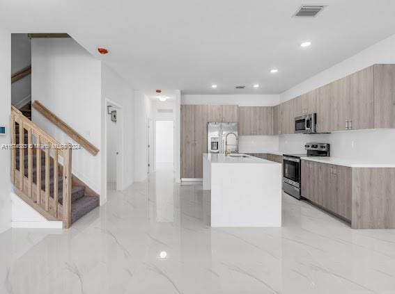 kitchen with a center island with sink, light brown cabinetry, sink, and stainless steel appliances