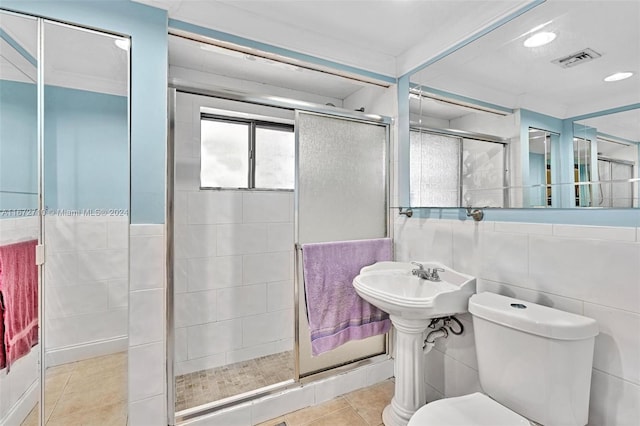 bathroom featuring tile patterned flooring, a shower with door, toilet, and tile walls