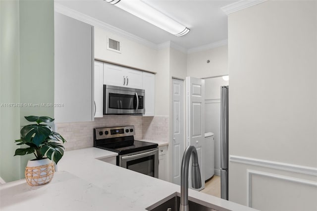 kitchen with appliances with stainless steel finishes, tasteful backsplash, light stone counters, crown molding, and white cabinets