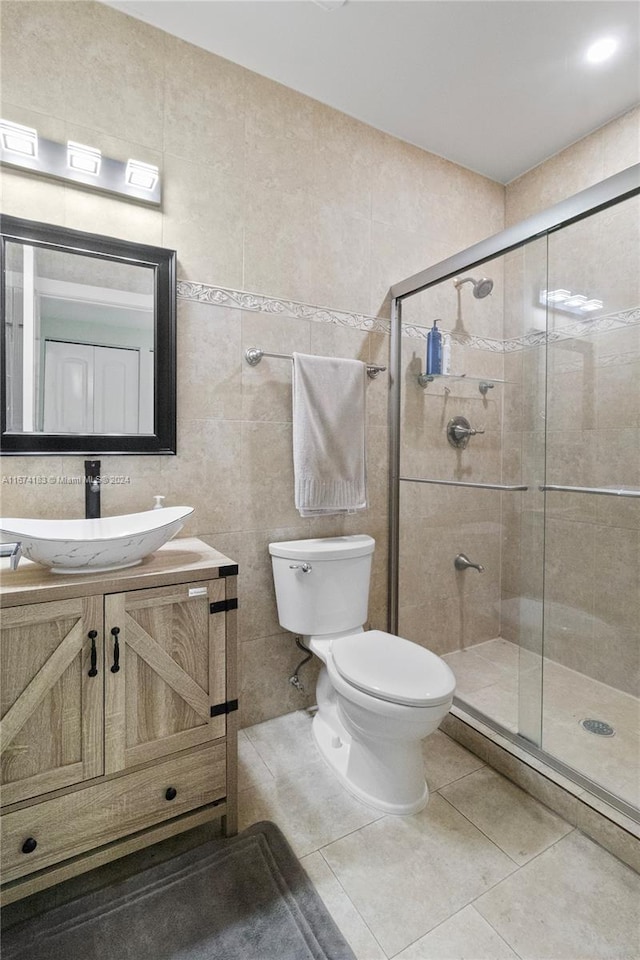 bathroom featuring vanity, a shower with shower door, tile patterned floors, tile walls, and toilet