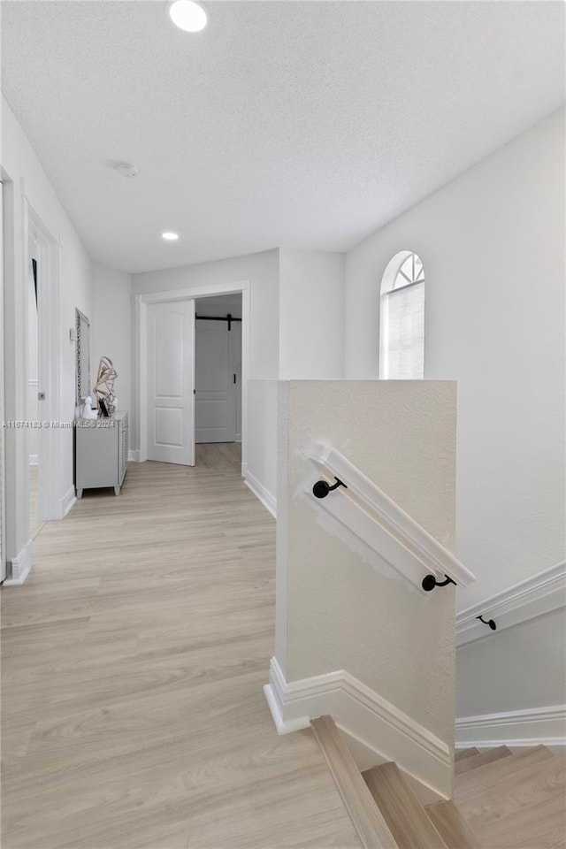 hall with a textured ceiling, light hardwood / wood-style flooring, and a barn door