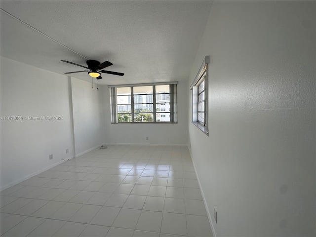 empty room with ceiling fan, a textured ceiling, and light tile patterned floors