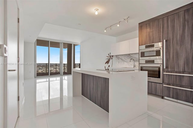 kitchen featuring light tile patterned flooring, stainless steel double oven, sink, backsplash, and white cabinets