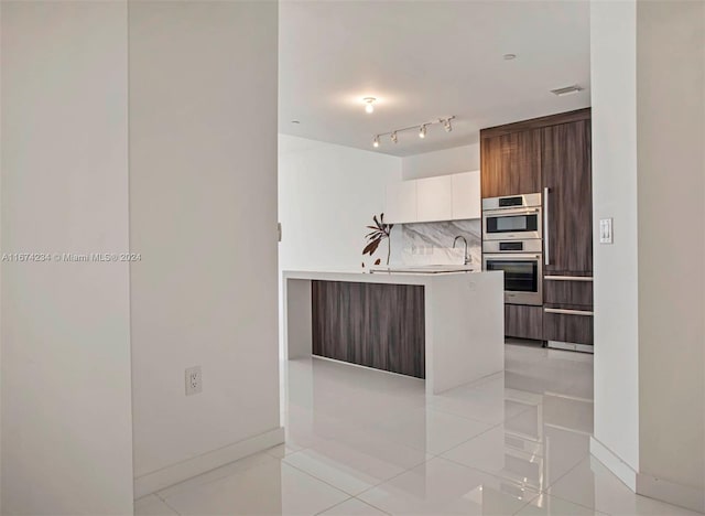 kitchen with light tile patterned flooring, stainless steel double oven, sink, decorative backsplash, and white cabinets