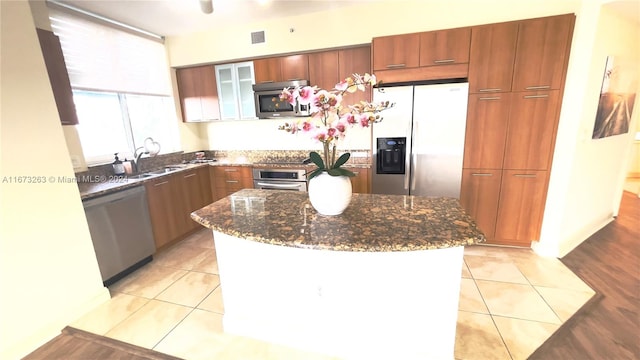 kitchen with appliances with stainless steel finishes, sink, a kitchen island, dark stone countertops, and light hardwood / wood-style flooring