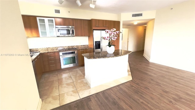 kitchen with a kitchen island, stainless steel appliances, light hardwood / wood-style floors, and dark stone counters